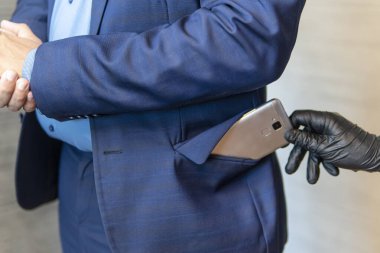 A gloved hand pulls out a mobile phone from a businessman's pocket. The concept of pickpocketing. The pickpocket is working. clipart