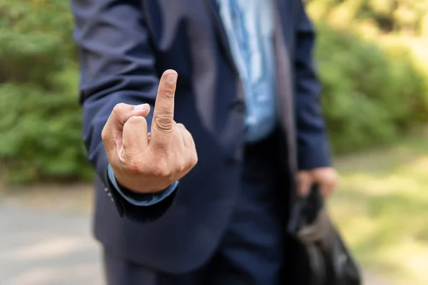 angry businessman showing middle finger outside office building. An indecent insulting gesture from a man in a suit. The businessman shows the middle finger.