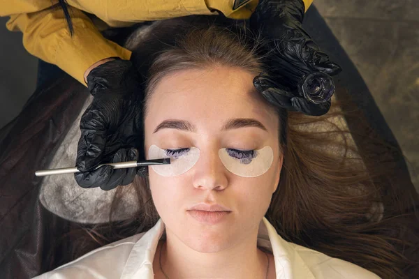 Kirpiklerini boyama prosedürüyle ilgili bir güzellik salonunda bir kız. Kaşlara ve kirpiklere dikkat et. Makyaj ustası müşterilerin kirpiklerini boyar. en üstteki görünüm