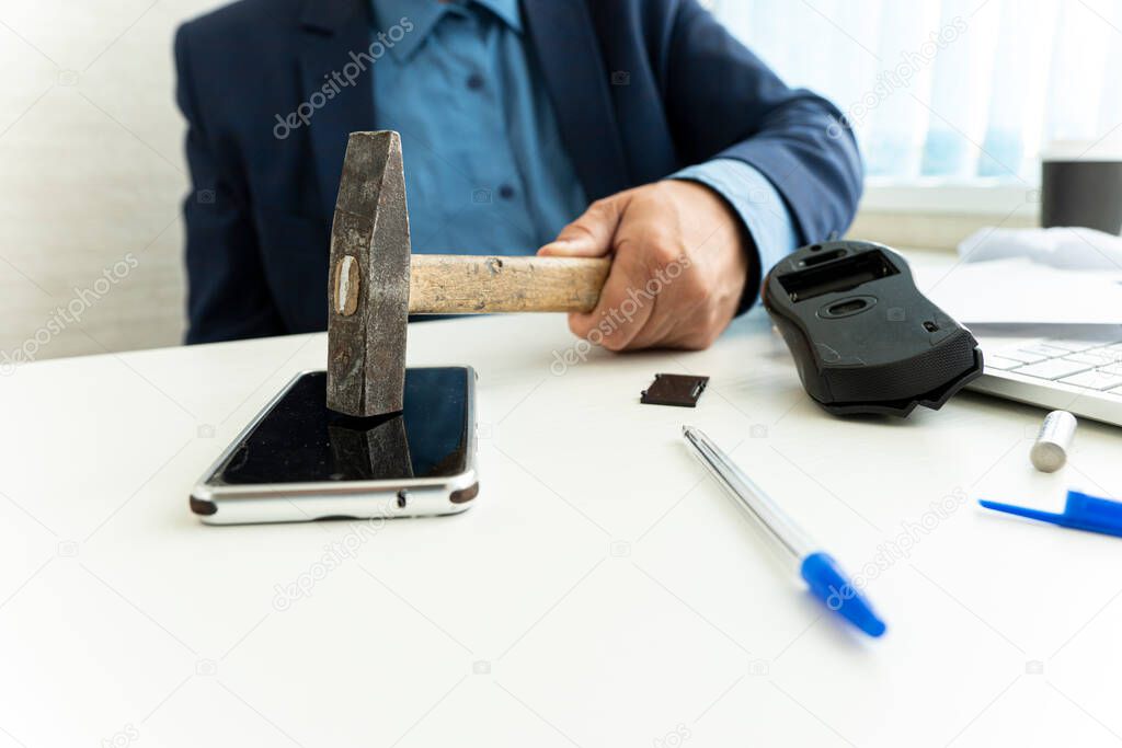 embittered businessman hits a smartphone with a hammer in workplace. Unsuccessful business negotiations concept. failure of the transaction.