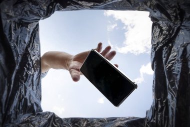 Adamın biri çalışmayan bir akıllı telefonu çöp kutusuna atıyor. Çöp kutusundan son görüntü. Çöplerle gezegenin geri dönüşümü ve kirliliği sorunu.