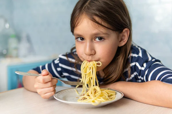 Kids eat pasta. Healthy lunch for children. Toddler kid eating spaghetti Bolognese in a blue kitchen at home. Preschooler child try noodles for dinner. Food for family.