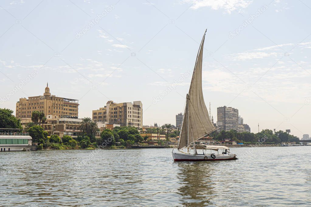 A sailboat on a river walk sails along the Nile River in the center of Cairo among the skyscrapers and attractions.