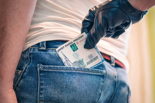 a black-gloved hand pulls the money out of his back pocket. The concept of petty crime and theft. Committing a crime, stealing money from the back of your jeans pocket, close-up