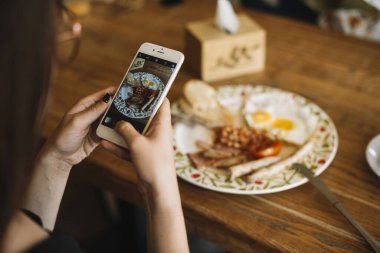 Kadının eli cep telefonuyla kahvaltılık ahşap masa fotoğrafı çekiyor. Yüksek kalite güzel fotoğraf konsepti