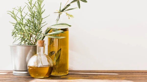 Rosmarin im Topf mit Olivenölflaschen Holztisch. Hochwertiges Foto — Stockfoto
