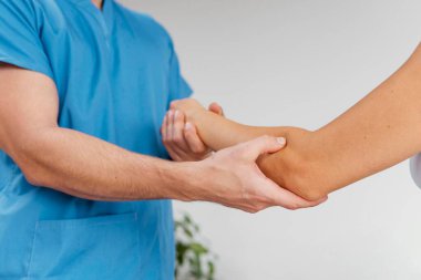Erkek osteopatik terapist kadın hastanın dirsek eklem hareketlerini kontrol ediyor.