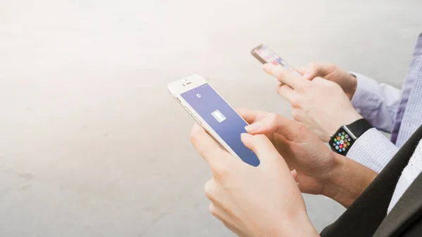 Женщина, использующая приложение facebook mobile рядом с мужчиной, носящим умные часы. Высокое качество фото — стоковое фото