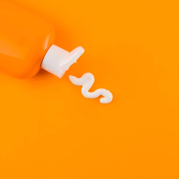 Crema blanca de protección solar saliendo botella naranja contra fondo naranja. Foto de alta calidad — Foto de Stock
