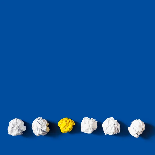 Żółta pognieciona papierowa kulka wśród białych kulek na niebieskim tle. Wysokiej jakości zdjęcie — Zdjęcie stockowe