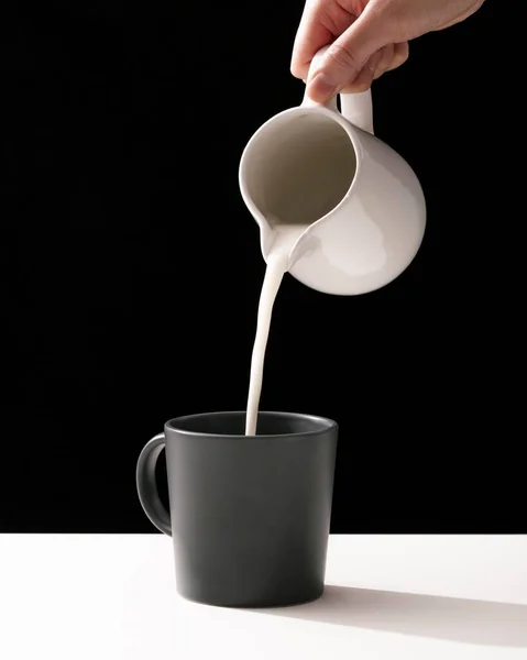 フロントビューの手でマグカップに牛乳を注ぐ。高品質の写真 — ストック写真
