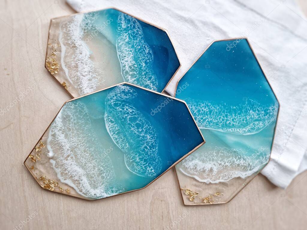 Resin coasters crystal form with sea waves pattern and golden edges. Blue geometric coasters set on white napkin. Table decoration