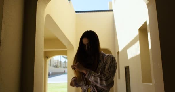 Dívka s dlouhými vlasy, česala si vlasy na ulici, v uličce mezi domy, ve stínu. Na pozadí slunečního světla, pomalý pohyb, detailní záběr — Stock video