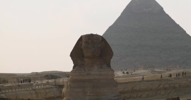 Reibungsloser Übergang von der Sphinx zur Großen Pyramide von Gizeh in Kairo, Ägypten. Klarer Tag, Touristen im Hintergrund. Weitwinkel, Zeitlupe — Stockvideo
