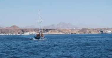 Eski ahşap bir gemi, pruva manzaralı, alçak yelkenli, körfezden çıkıyor. Sharm El Sheikh limanının manzarası, çöl, kum, iskele..