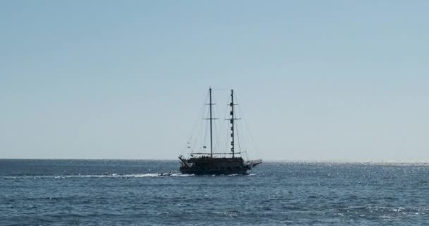 Un antiguo barco de recreo con turistas y velas bajas, arrastrando un bote inflable detrás de él contra un cielo azul claro. Disparo muy amplio, cámara lenta — Vídeo de stock