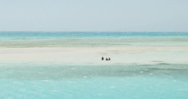 Kızıl denizin ortasında, çok güzel turkuaz suların arasında, Ras Muhammed 'in Beyaz Adası' nda suda oturan turistler. Açık bir gün, küçük dalgalar. Geniş çekim, yavaş çekim..