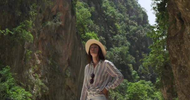 一个戴着帽子的女孩在一个绿树成荫的峡谷里看了看四周.看起来很害怕很震惊在阿尔巴尼亚的Gjipe峡谷失踪晴天，慢动作 — 图库视频影像