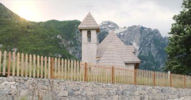 Alplerdeki ahşap çatılı eski bir kilisenin sihirli manzarası. Karla kaplı dağlar, yeşil ağaçlar, kar yağışı, batan sarı güneş. Orta boy, öğleden sonra güneşi.