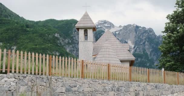Vue d'en bas sur une église en Albanie, Theth. De jour, sur le fond des Alpes avec de la neige. Clôture en bois, nuageux. — Video