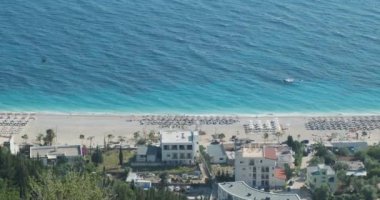 Arnavutluk 'ta küçük bir tatil köyünün şemsiyeleriyle sahilin en üst manzarası. Mükemmel manzara, mavi ve turkuaz deniz. Geniş açı, güneşli gün