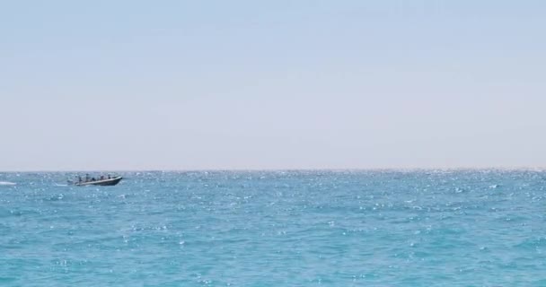 Motorówka z ludźmi poruszającymi się szybko wzdłuż powierzchni morza, cięcia fal, tworząc pianę po sobie. Albania, jasny słoneczny dzień, szeroki strzał. — Wideo stockowe