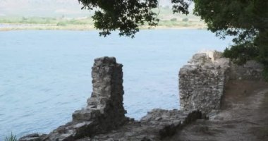 Arnavutluk 'un Butrint Park kentinde antik bir duvar ve göl manzarası. Orta boy, gündüz vakti, ağaç gölgesi.