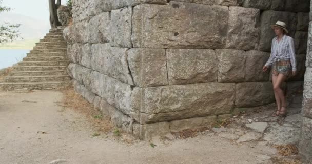 Una donna esplora le antiche rovine della città di Butrint in Albania. Passa vicino a un muro di pietra, passa la mano sulle pietre. Di giorno, inquadratura ampia — Video Stock