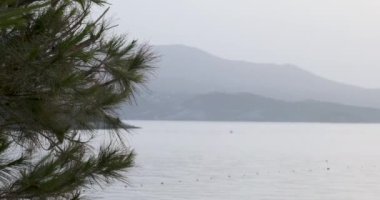 Arnavutluk 'un sakin deniz manzarası, Ksamil. Hafif bir sis bulutu içinde dağların manzarası ve hareket eden küçük bir motorlu tekne ile sahil şamandıraları. Panorama, geniş açı..