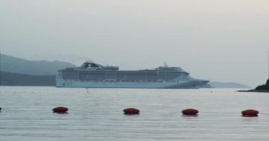 Büyük bir yolcu gemisi adaların arka planına karşı küçük bir körfezde yelken açıyor. Akşam vakti, kıyıdan manzara, geniş açı. Arnavutluk, Ksamil