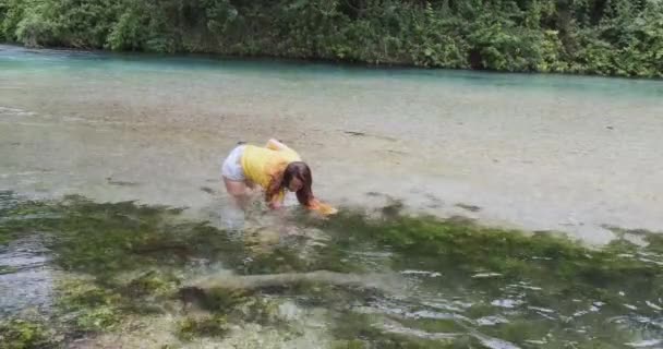 Mujer saca botellas de basura del fondo del río, tiradas al agua. Agua turquesa transparente. Durante el día, tiro ancho — Vídeos de Stock