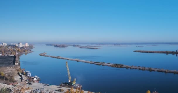 Panoramic view from the top of the industrial part of the city with cranes and heaps of coal. Against the backdrop of a beautiful calm expanse of the river and a cloudless sky with many islands — стоковое видео