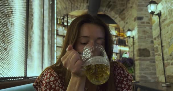 Самотня молода жінка, яка чекає когось у пабі і п'є пиво. Крупним планом, в приміщенні — стокове відео