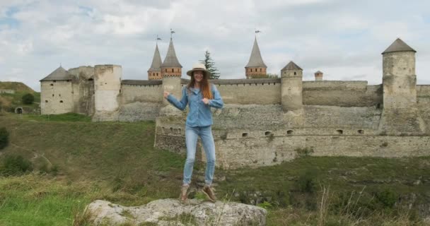 Fiatal lány ugrál és táncol a háttérben egy régi kastély. Nappali, táv lövés, Kamenetz Podolsk erőd. — Stock videók