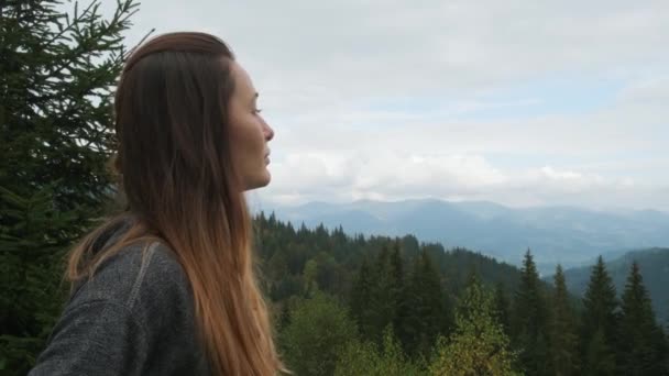 Belle fille aux cheveux longs dans la forêt des Carpates parmi les sapins, tourne la tête et regarde au loin les montagnes. Gros plan, ralenti, diurne — Video