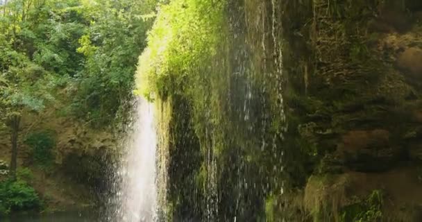 水流从布满绿色苔藓的悬崖上从上到下落入一个小泻湖. — 图库视频影像