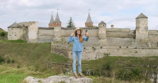 Woman takes a selfie in front of a beautiful old castle. Kamenets Podolsky, Ukraine, wide shot, daytime — Stockvideo