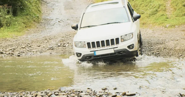 White SUV overcomes a mountain river ford. Forest muddy rocky road, extreme car trip in Carpathians, Ukraine. — Stockfoto