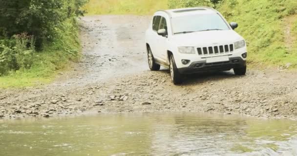 White SUV overcomes a mountain river ford. Forest muddy rocky road, extreme car trip in Carpathians, Ukraine. — Wideo stockowe