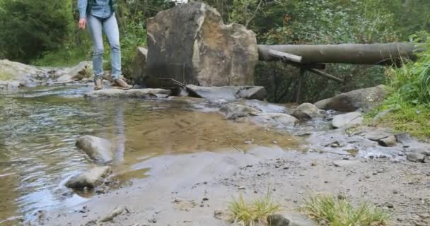 Female tourist crosses a small mountain river, stops to wash his face with cool water to refresh himself. Then he continues his journey with a backpack. Spring, summer, wide shot, slow motion — Αρχείο Βίντεο