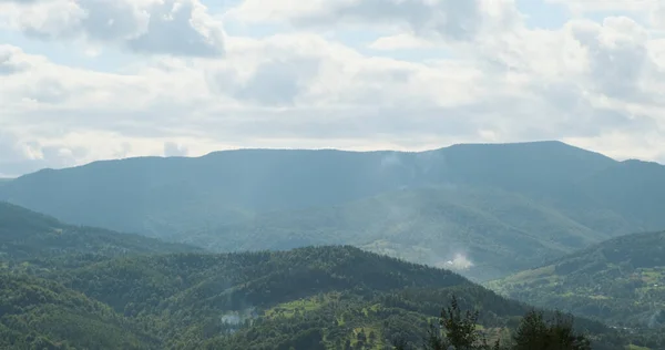 Vista sulle montagne con nuvole bianche, tra verdi zolmi ricoperti di foresta. La bellezza e la tranquillità della natura. Ampie riprese, giorno, primavera, estate — Foto Stock