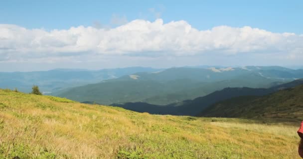 Girl with a backpack climbs a mountain. Side view, clouds and windy weather, green grass, beautiful view of the Carpathians. Medium shot, daytime, spring summer. — Stok Video