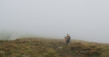 Büyük sırt çantalı iki turist yoğun siste dağın tepesinden iniyor. Yüksek bulut, görülecek bir şey yok.