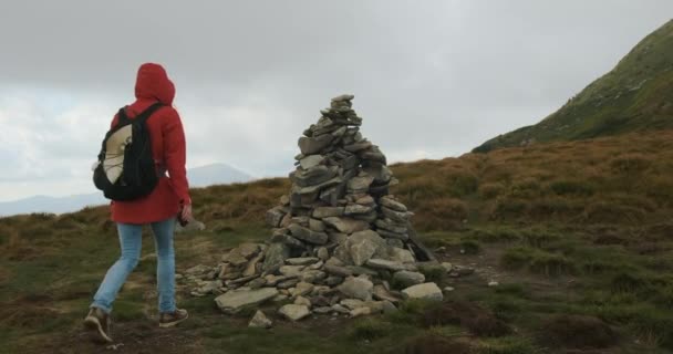 Female tourist with a backpack, puts a stone in the cairn on the mountain. Bad weather, fog. Carpathians, Ukraine, Europe. — Stockvideo