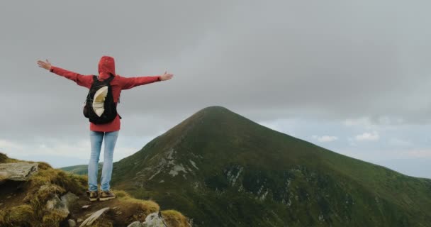 Woman, having reached the top, looks at the mountain in the fog and spreads her arms to the sides. Achieving the goal, conquering the summit. Carpathians, Ukraine, daytime, cloudy. — Vídeo de stock