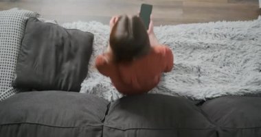 Genç bir kadın kanepeye oturur ve yeşil ekranda telefonu kullanmaya başlar. Ekrana dokunmak, çevrimiçi internet, gezinmek. Üst görünüm, kapalı alan, orta çekim.