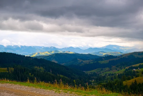 Blick auf die Berge, eine große graue Wolke hängt am Himmel und erzeugt einen Schatten über den grünen Waldhügeln. Frühlingssommer in den Karpaten, Ukraine. — Stockfoto