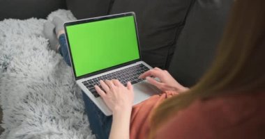 Kadın kanepeye uzanıyor ve çalışıyor. Laptopun arkasında parmak izleri, yeşil bir ekran. Evden çalışma konsepti, serbest çalışan, iletişim, uzak işyeri, rahat ev ofisi.