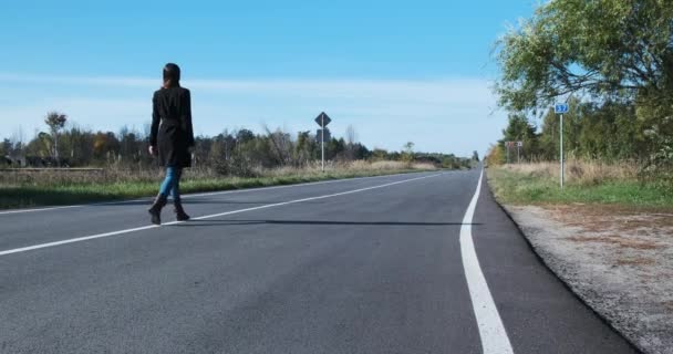 Flicka går längs en tom asfalterad väg i Tjernobyl, uteslutningszon, spökstad. Det finns ingen. Kvinnan går sin väg. Dagtid, vårsommar. Utflykt till Pripyat. — Stockvideo