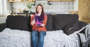 Oturma odasındaki koltukta oturan kadın akıllı telefon ekranındaki hologramdan ayakkabılarını seçiyor. 3D ayakkabılar telefon ekranında dönüyor, el ayakkabı modellerini dalga dalga değiştiriyor. Metaevren